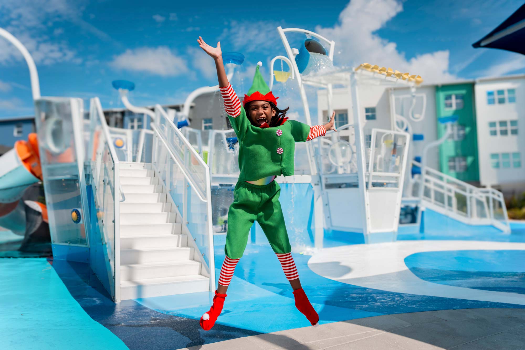 person in elf costume jumping in front of a splash park